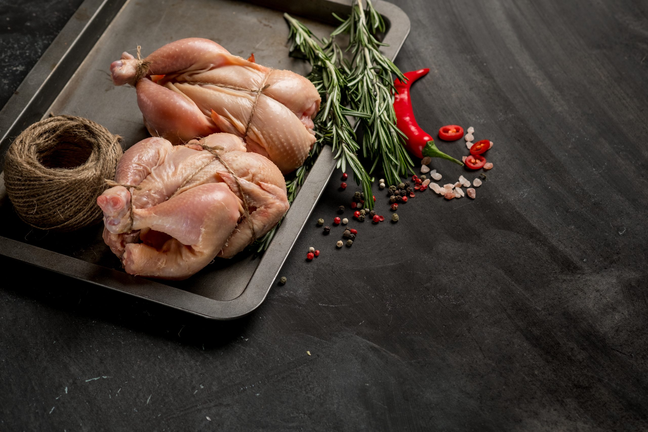 Young chicken on a baking sheet with seasonal vegetables and greens before baking in the oven. Photo of food on a dark background for a book of recipes or design. Horizontal view.